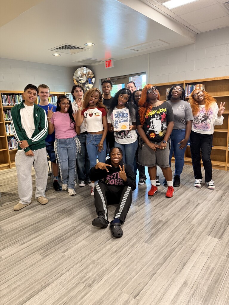 Group of young people in a library, some wearing sneakers, others in boots, standing and posing.