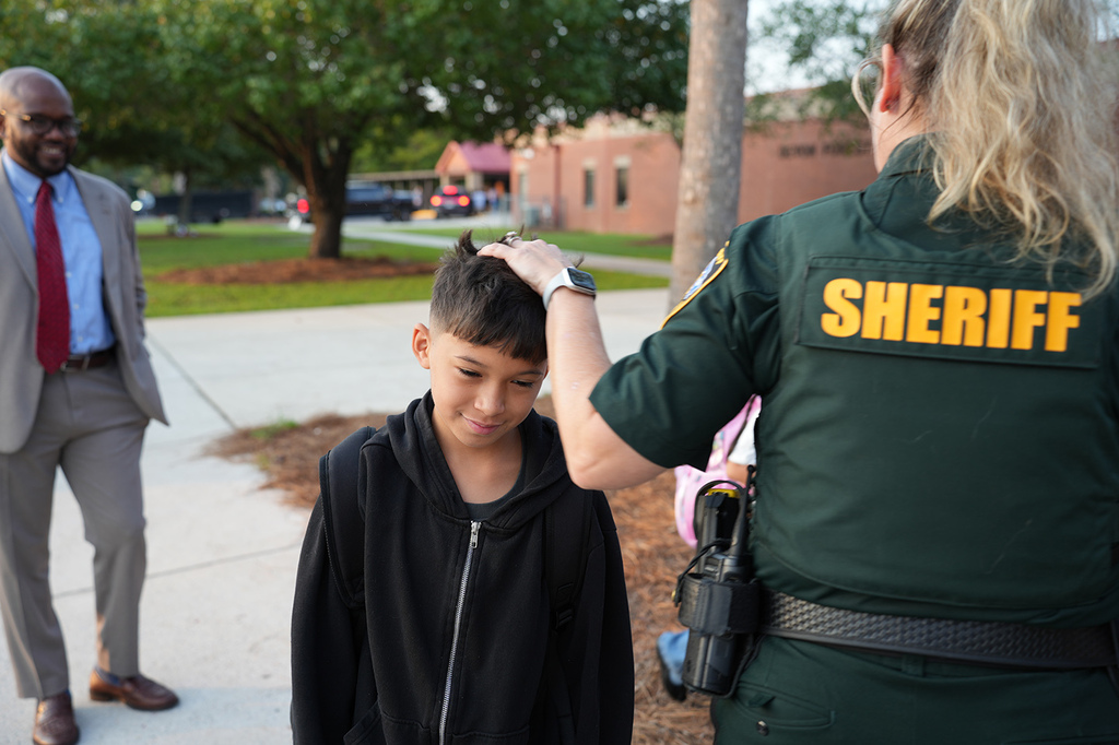 A uniformed female officer places her hand on a young boy's head while another man in a suit watches.