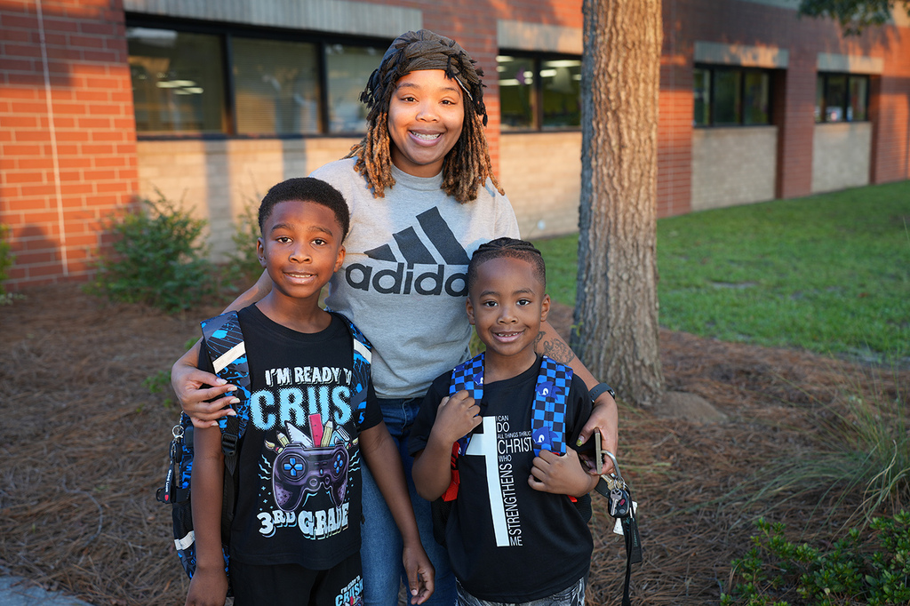 A woman and two children pose for a photo in front of a brick building. They are smiling.