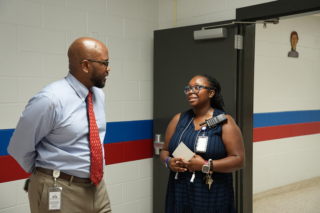 An adult man in a tie and a woman in a dress stand near a door with red, white, and blue stripes.
