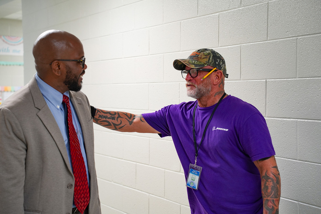 Two men facing each other, one wearing a suit and tie, the other in a purple shirt and cap.