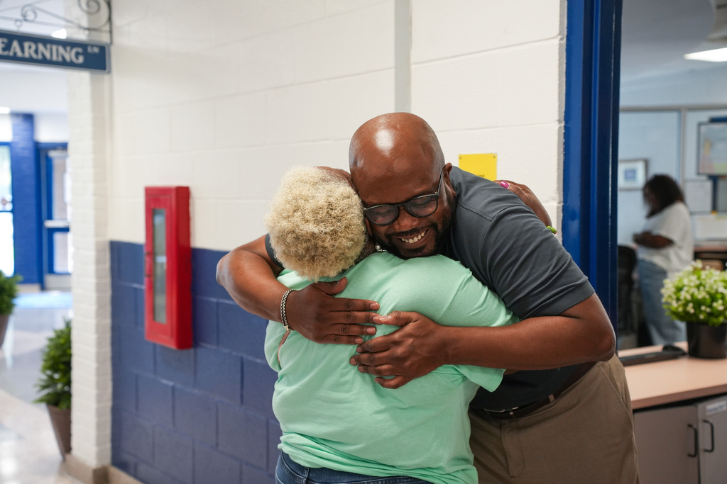 Man and woman embracing in hallway. Blue and white walls. A person stands in the background.