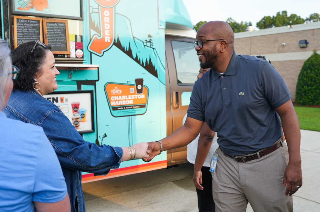 Three people engage in conversation near a food truck, with one man shaking another's hand.