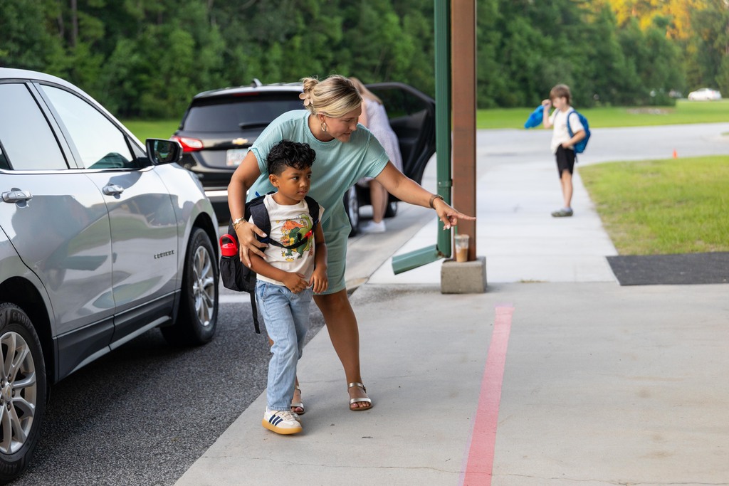 Woman with a child on a sidewalk, guiding him to cross the street near cars.