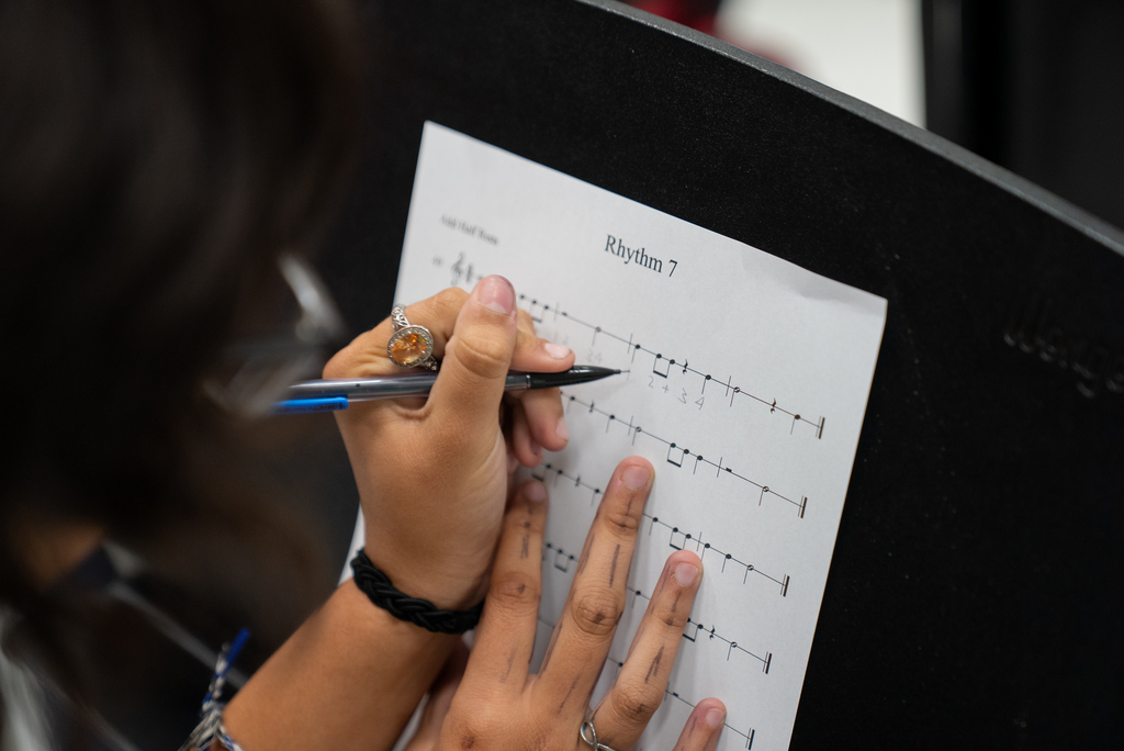 Person with a pen, writing on a music sheet. The paper reads "Rhythm 7".