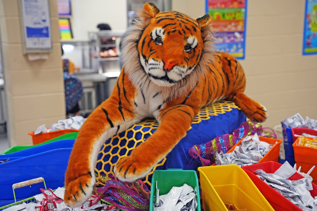 A large stuffed tiger sits on a blue cushion amidst a variety of colorful bins.