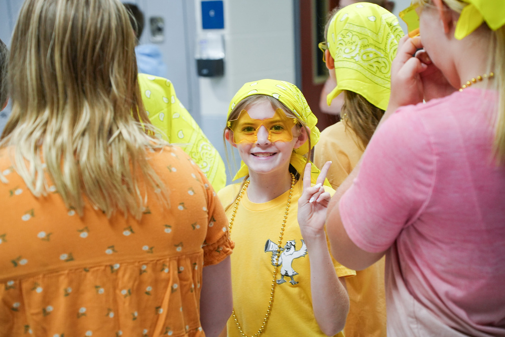 Group of people in bright yellow, smiling and interacting. One child has yellow painted around eyes.