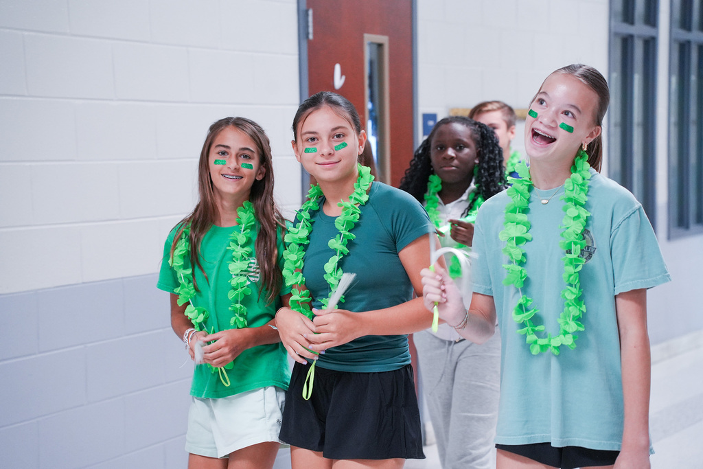 Four girls with green face paint and green leis pose in a hallway with a white wall.