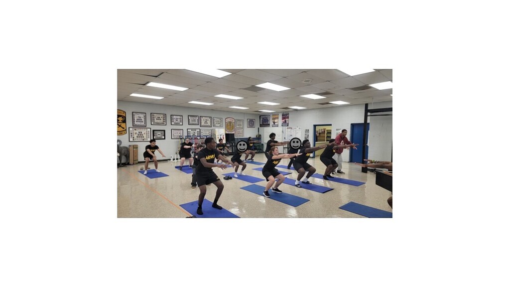 A group of people doing yoga in a room with mats on the floor, under white ceiling lights.