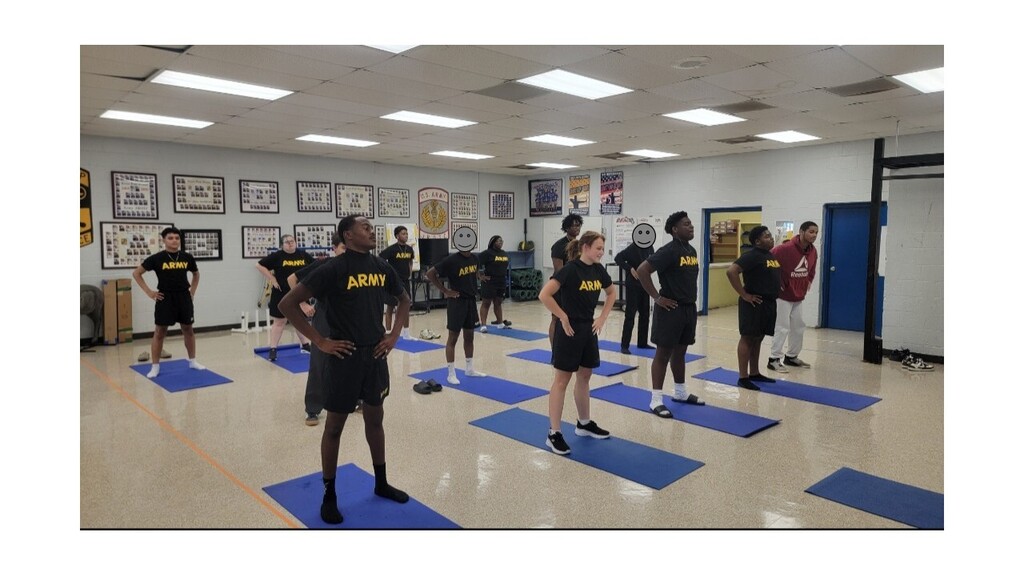 A group of people dressed in black uniforms with "Army" on the back, doing yoga on blue mats.