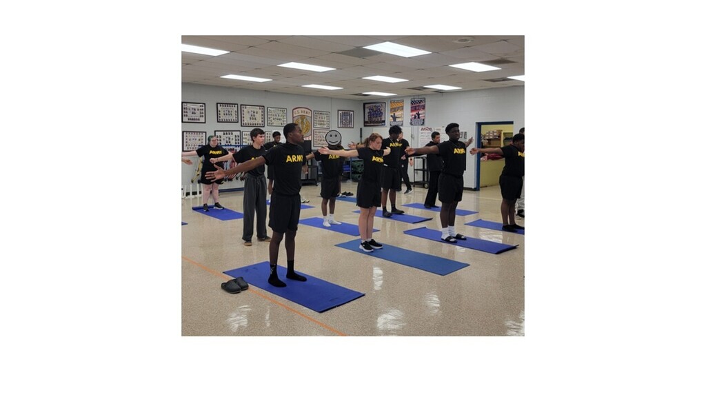 Group of people in black shirts and shorts performing yoga poses in a room with blue mats.