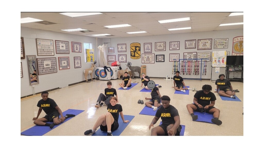 Group of individuals in military uniforms practicing yoga on blue mats in a room with framed artwork on walls.