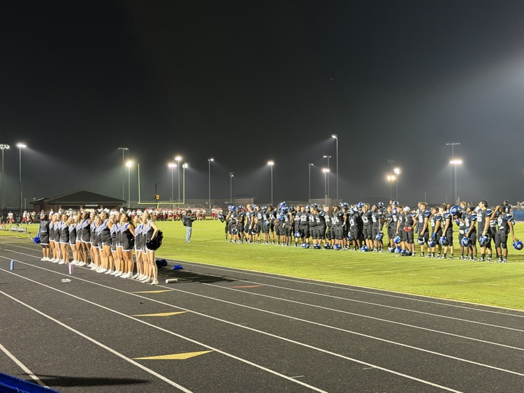 Cane Bay football players and cheerleaders stand together on the field under the stadium lights.