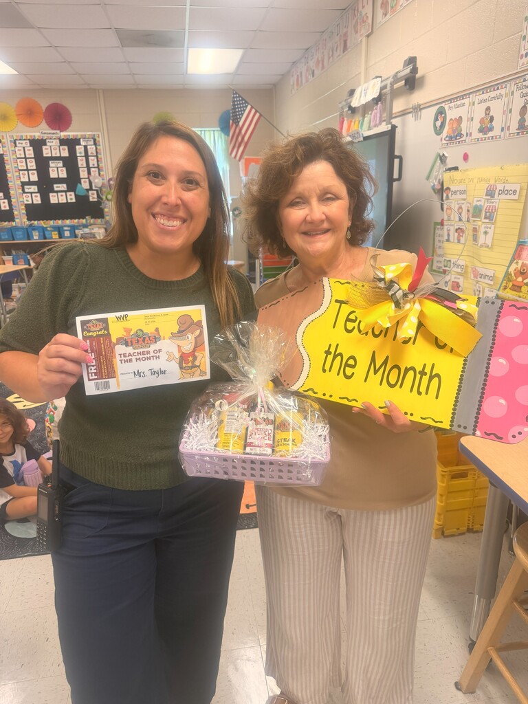 Two women pose with gifts in a classroom. One holds a certificate and the other a box.