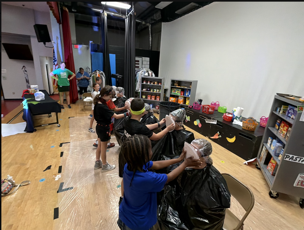 Multiple children in a room, washing and styling a person's hair in a plastic bag.
