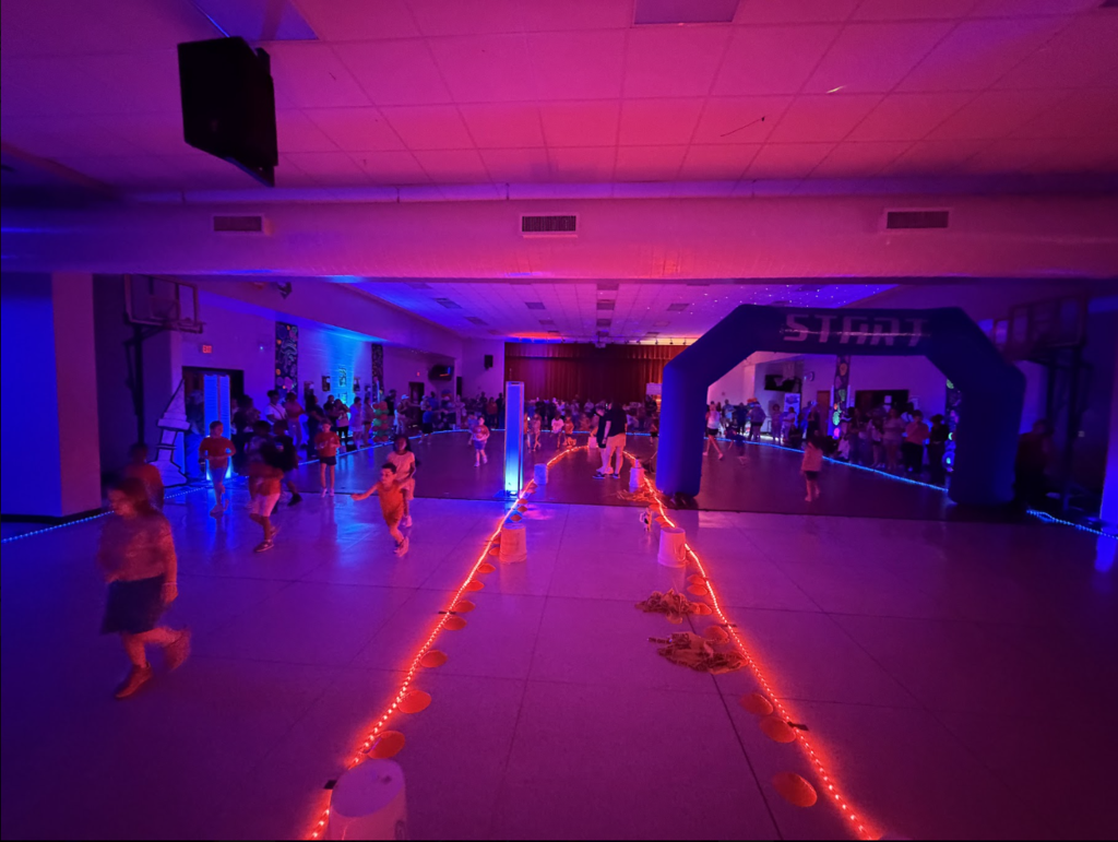 A gymnasium with children running on a track. Bright red and purple lights are on the floor.