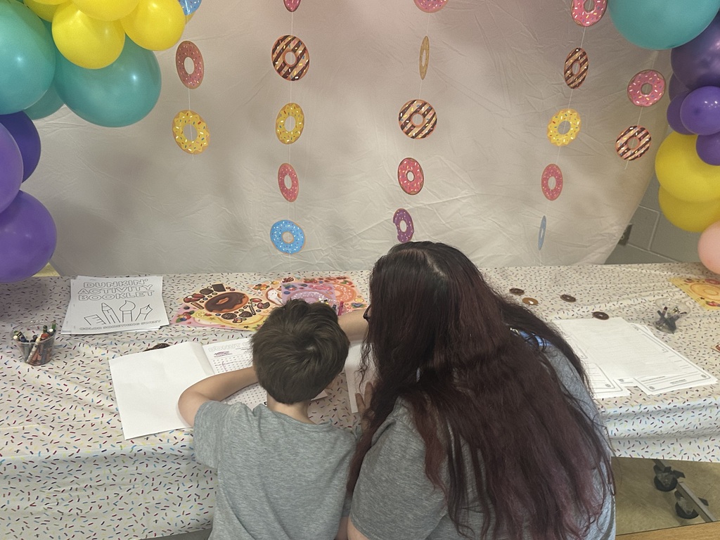 A table with paper, pens, and a colorful donut display. A woman and a boy sit there.