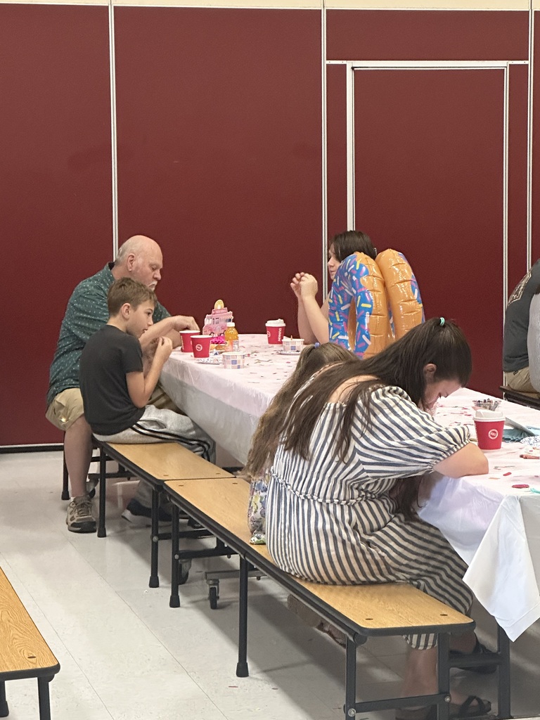 Several people sitting at a table with a white tablecloth and red cups. Two long benches are present.