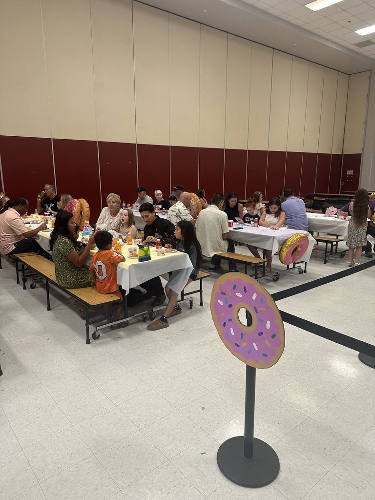 Several people sit at tables in a room with red walls. Tables are covered in white cloths.