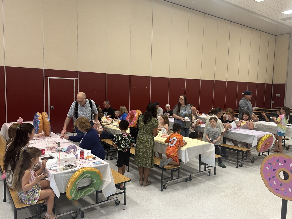 A room with a red wall. A group of adults and children are gathered around tables.