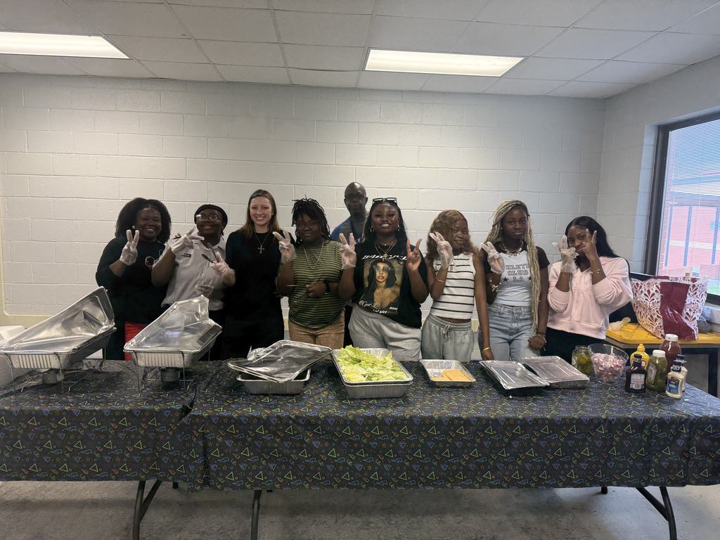 Group of individuals posing behind a long table covered with food, some showing peace signs.