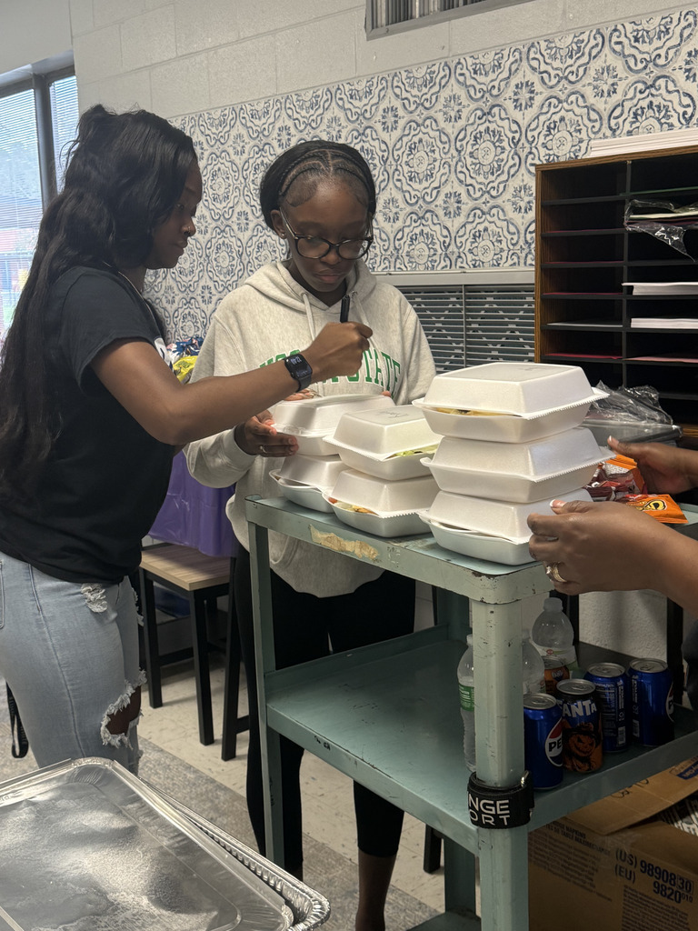 Two women in a room prepare food. One wears glasses and a hoodie. The other, a watch and jeans.