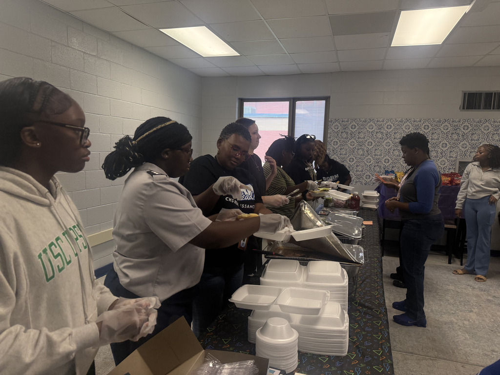 Group of people in a room with white walls serving food at a long table.