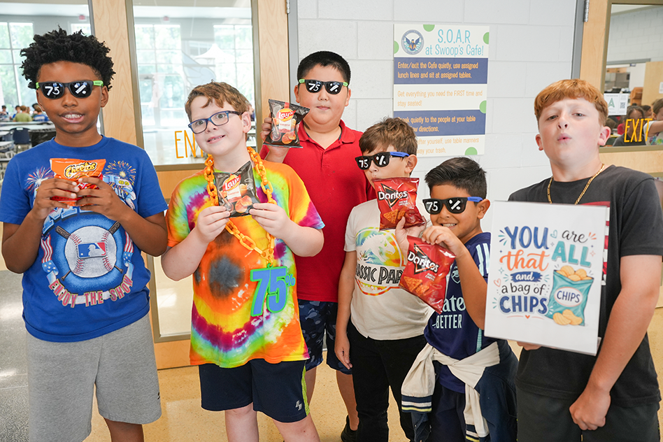 Five young boys hold snacks. One holds a sign with "You are that all of chips" in front.