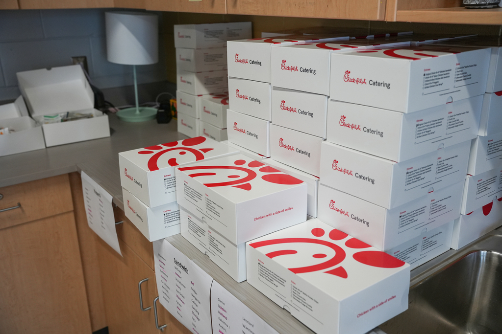 Stack of white boxes with red logos in a kitchen. Cabinets and a sink are in the background.