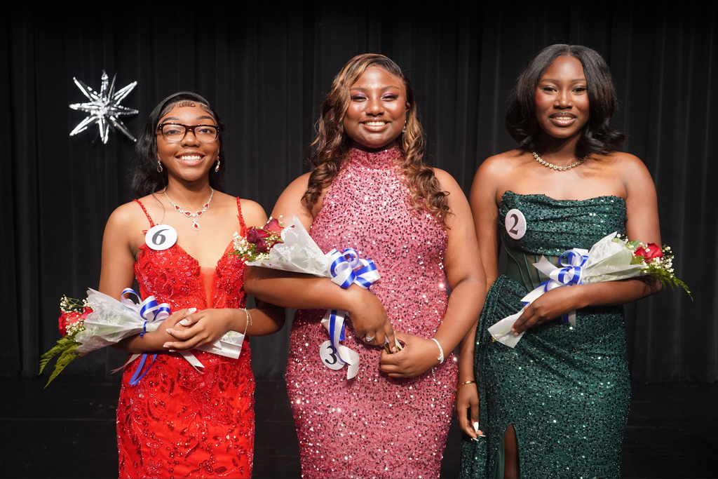 Three women, likely pageant contestants, stand on stage, each holding bouquets. One wears red, another green, and the third pink.