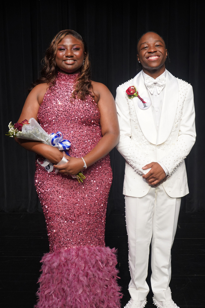 A woman in a pink dress holding flowers and a man in a white suit standing together on a stage.