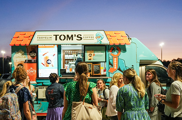 People stand in line outside a Tom's Coffee food truck with a colorful design.