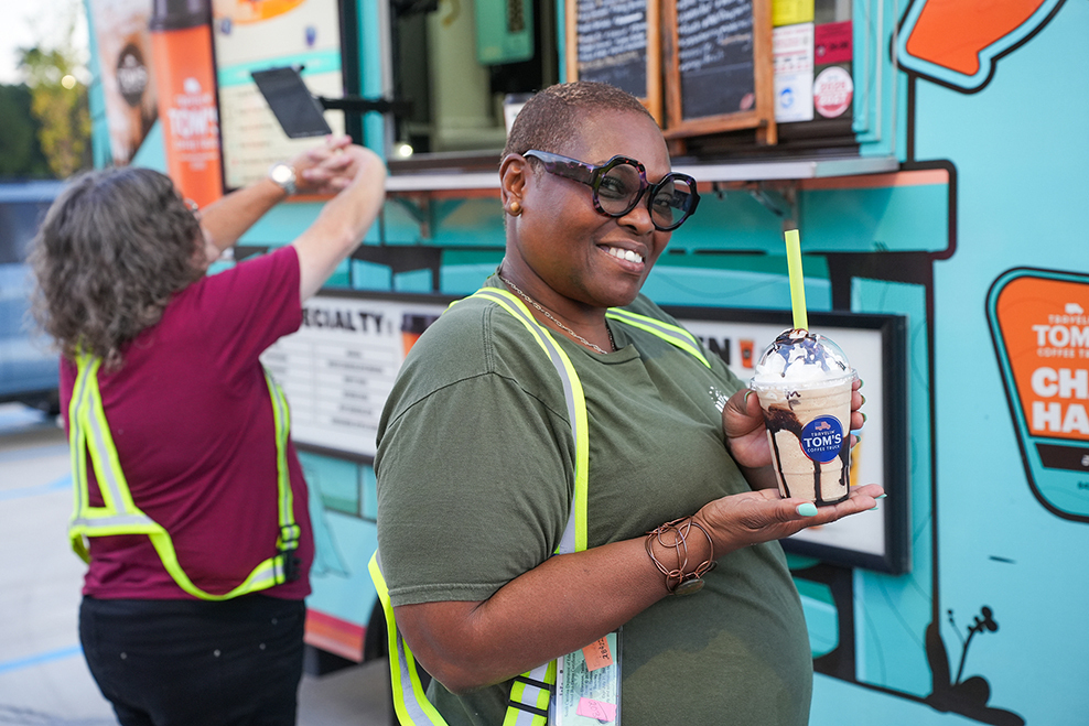 A woman smiles while holding a drink in a food truck. Another person stands behind her, holding a menu.