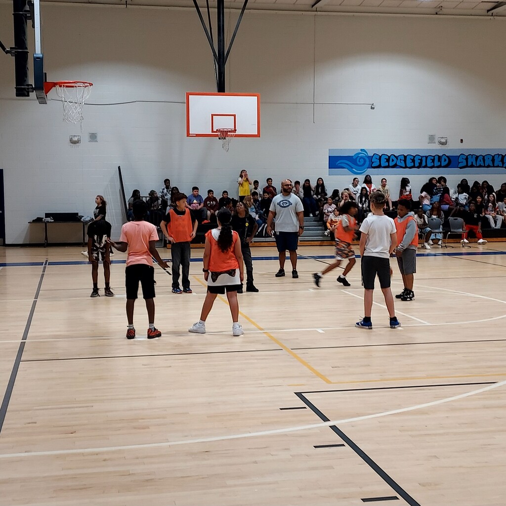 A basketball court with players and spectators. The players wear numbered jerseys and sneakers.