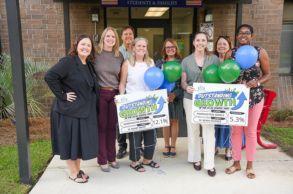 A group of women holding signs with balloons, standing in front of a brick building entrance.