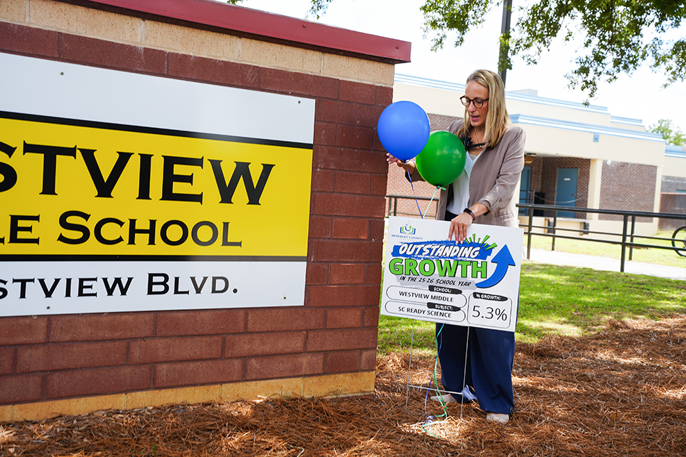 A woman holds two balloons in front of a sign for Westview Elementary School.