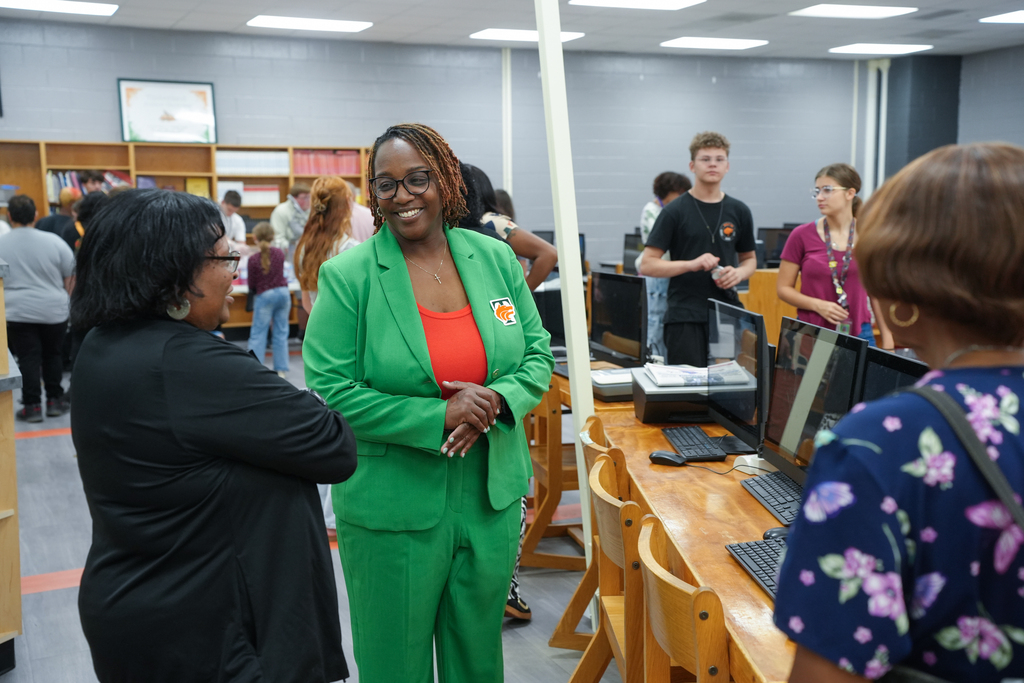A woman in a green suit stands among others in a room with computers and desks.