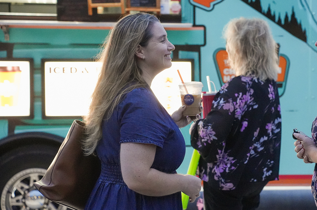 Two women, one with long blonde hair in a blue dress, holding a cup, the other with blonde hair in a black floral dress.