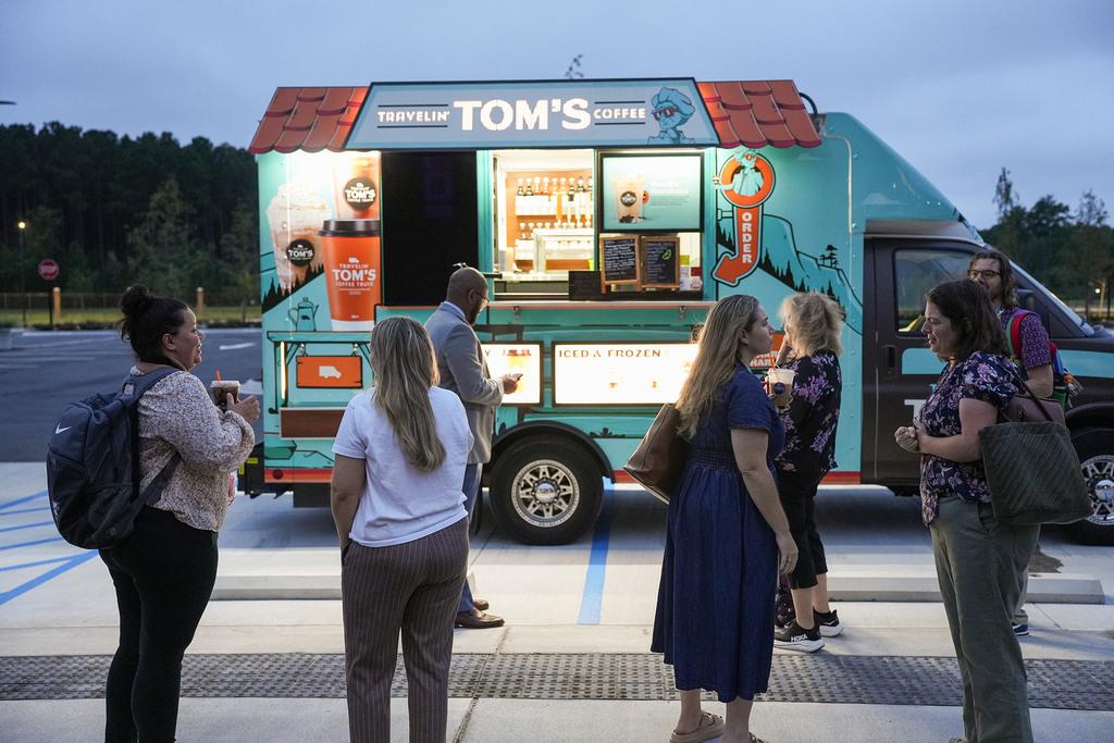 People stand in front of a blue mobile coffee truck with "TOM'S COFFEE" written on it.