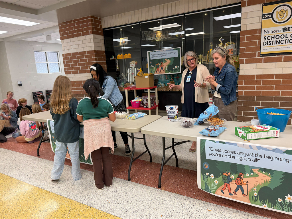 People stand at tables in a room, displaying items. Banners hang on walls. People sit on the floor.