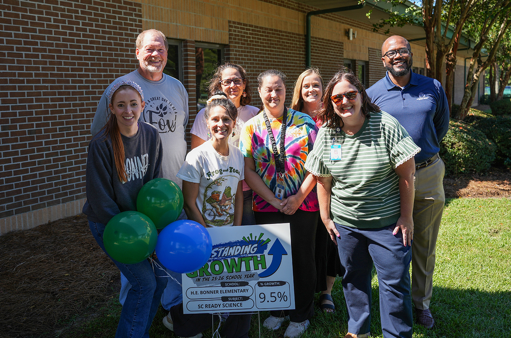 Group of adults and children posing for a picture in front of a building. Some hold balloons.