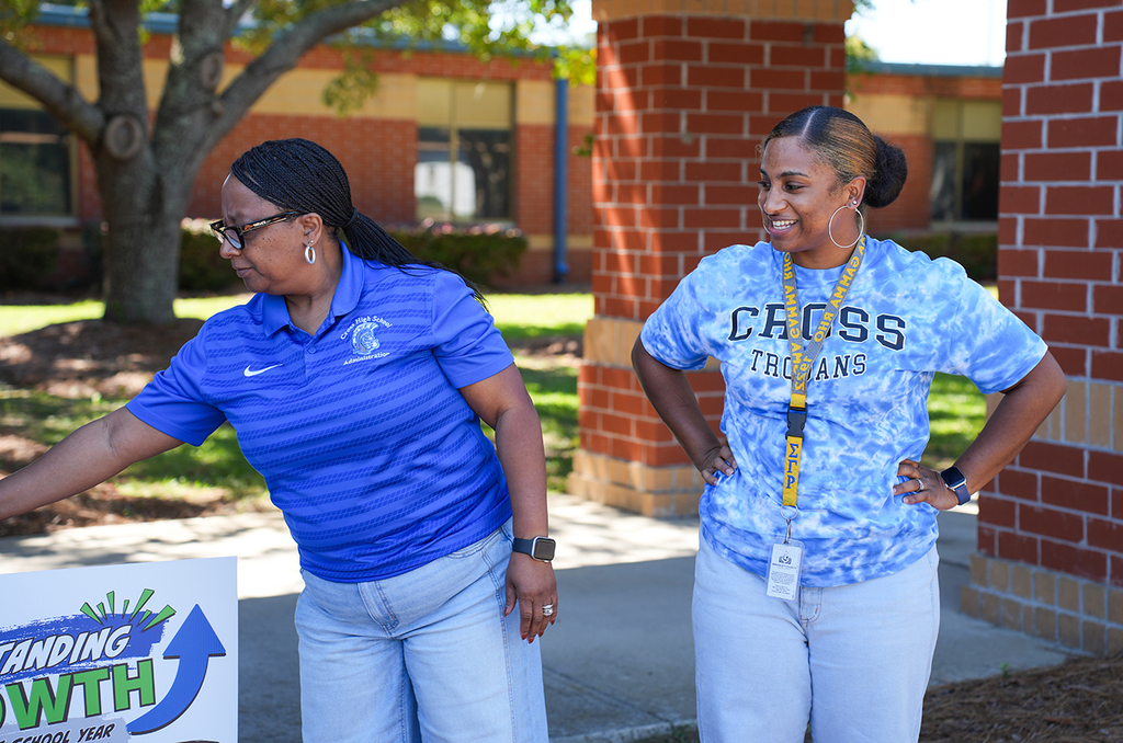 Two women, one in a blue shirt and the other in a white shirt, stand outside a brick building.