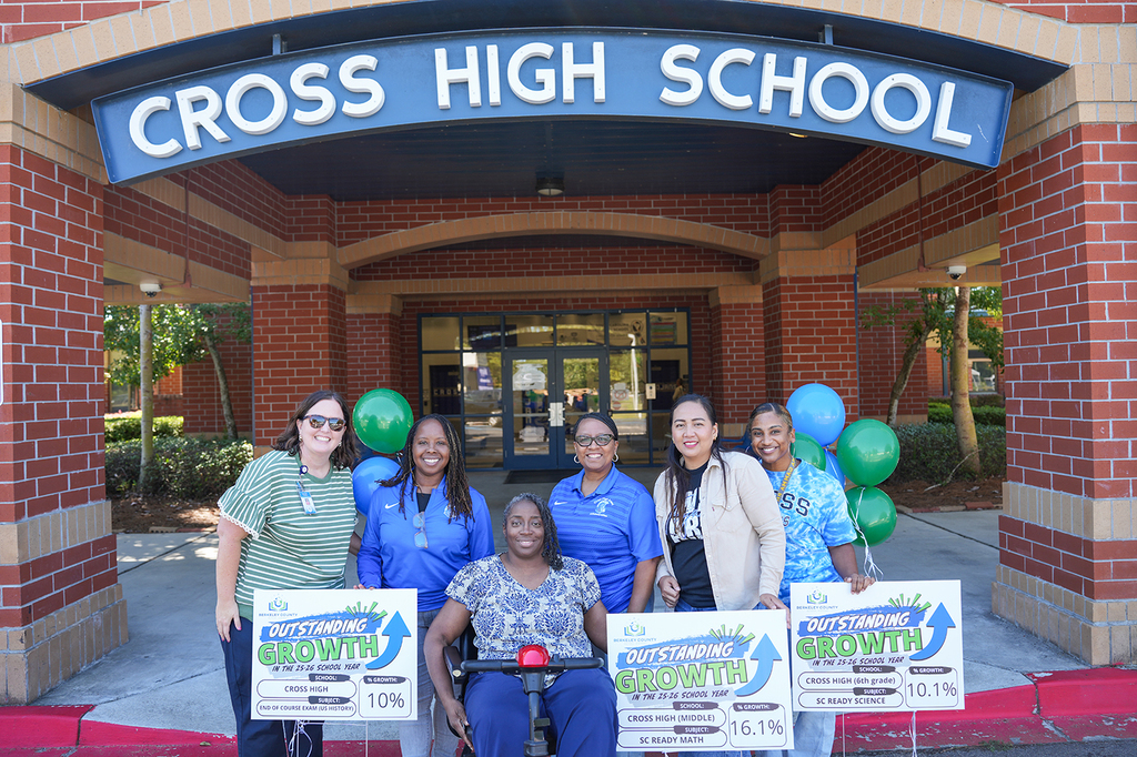 A group of people holding signs stands outside Cross High School. A woman in a wheelchair sits in the center.