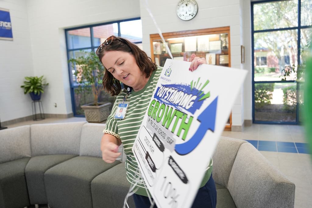A woman adjusts a sign that reads "Outstanding Growth" in a room with glass windows and a couch.