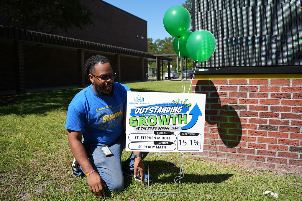 Person kneels by a sign with a green arrow pointing up and balloons. A building is in the background.