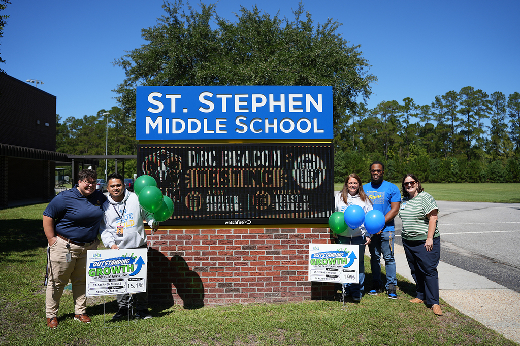 Group of people standing behind a brick sign that says St. Stephen Middle School. They hold signs and balloons.