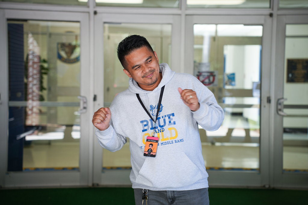 Man in a white hoodie with "Blue Gold" text standing in front of a building with glass doors.