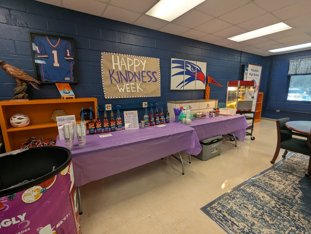 Room with blue walls and a large sign reading "Happy Kindness Week". Two tables covered in purple cloth.