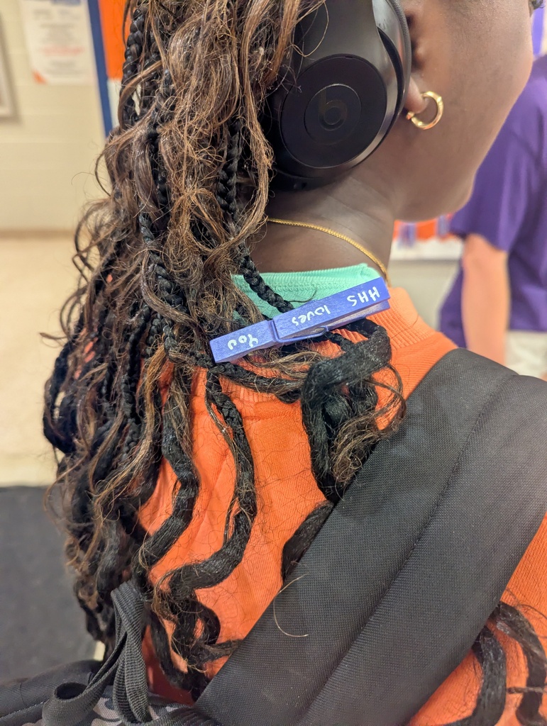 A person with curly hair wearing an orange shirt, headphones, and a blue name tag.