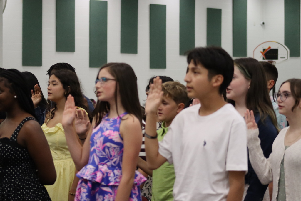 Students stand in a line, with arms at sides, hands over hearts, and reciting the Pledge of Allegiance.